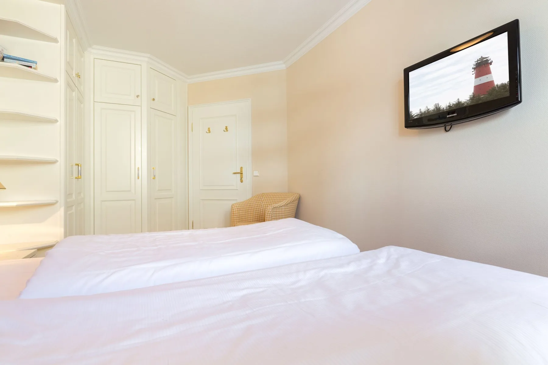 Dormitorio con dos camas, armarios empotrados y un televisor en la pared.