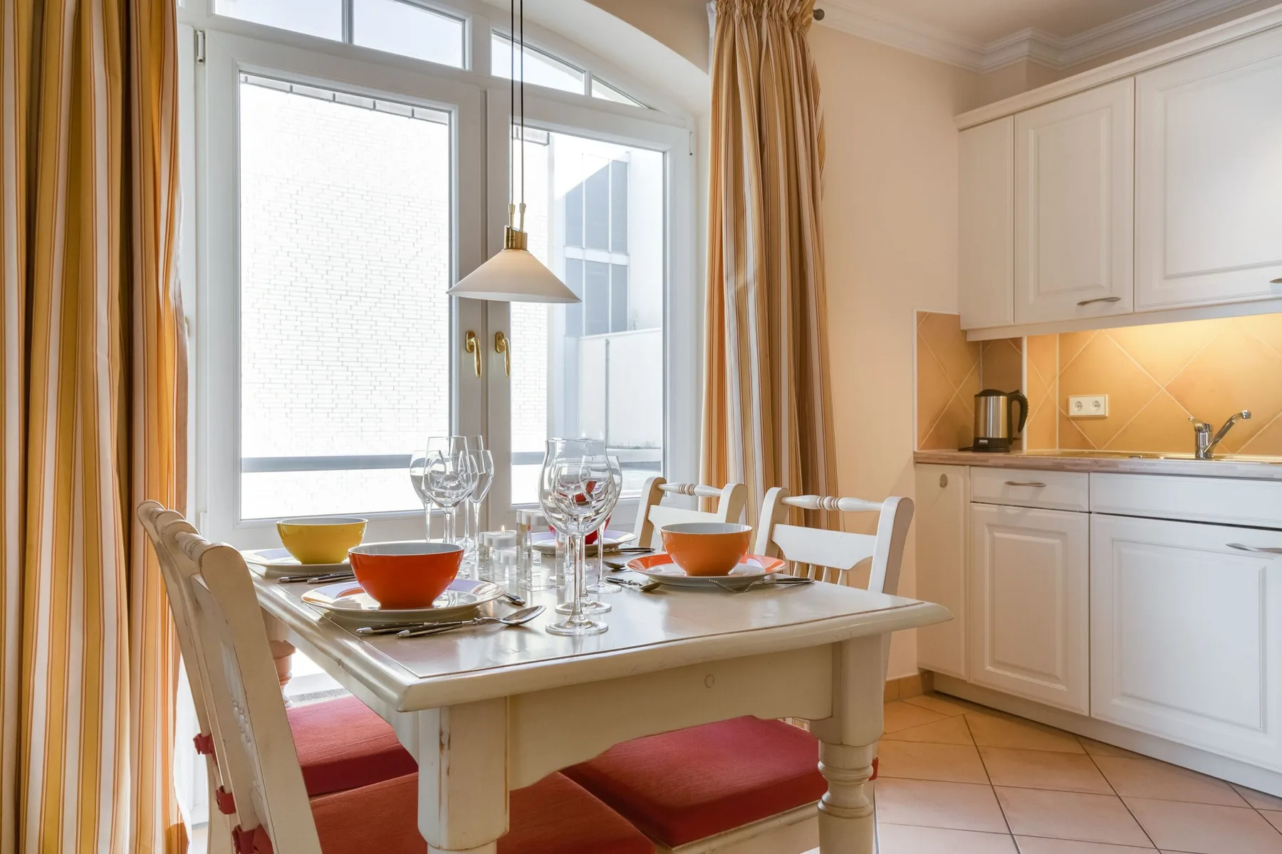 Una mesa de comedor está puesta junto a una ventana luminosa en una cocina.