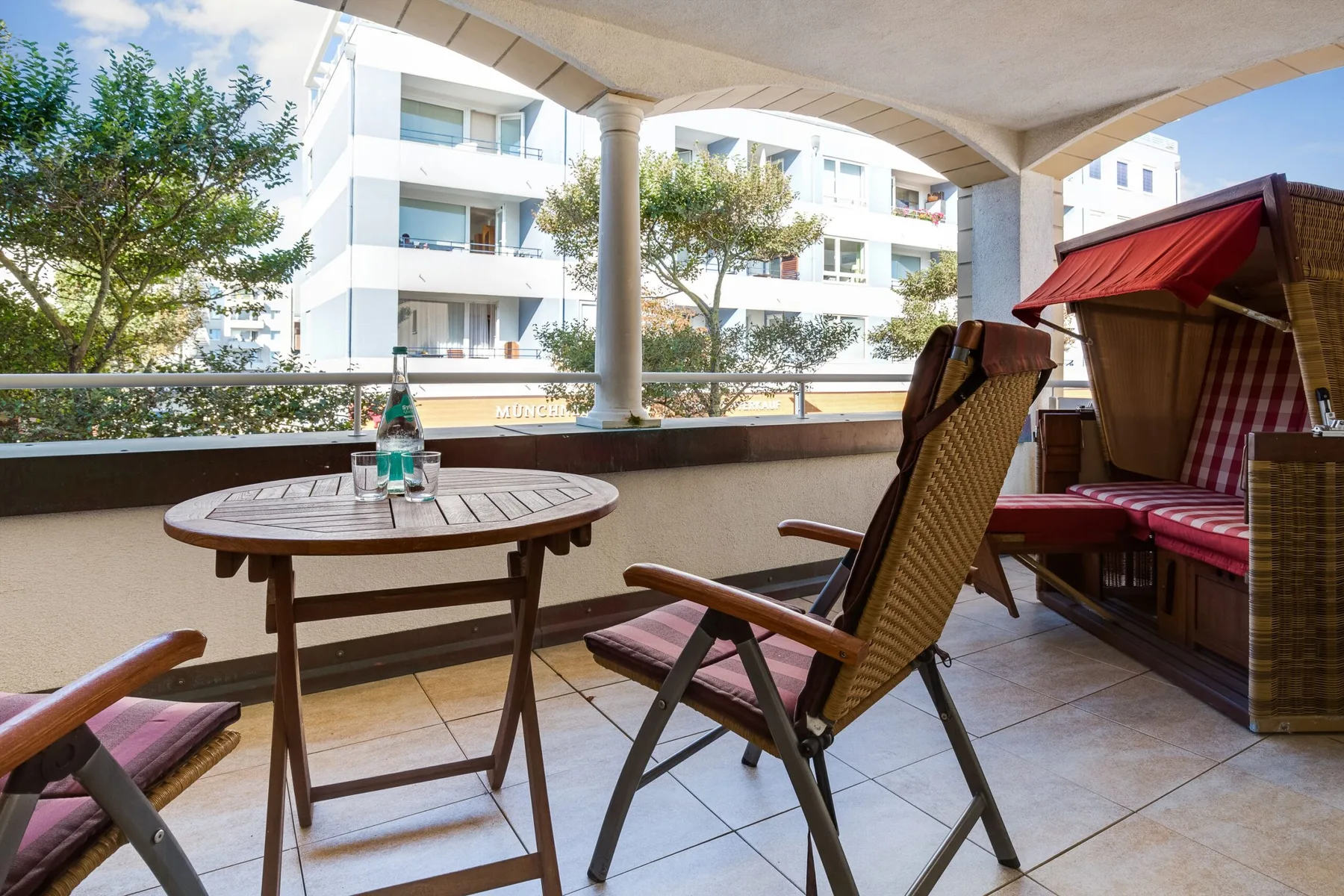 Una terraza cubierta con asientos al aire libre da a un edificio de apartamentos cercano.
