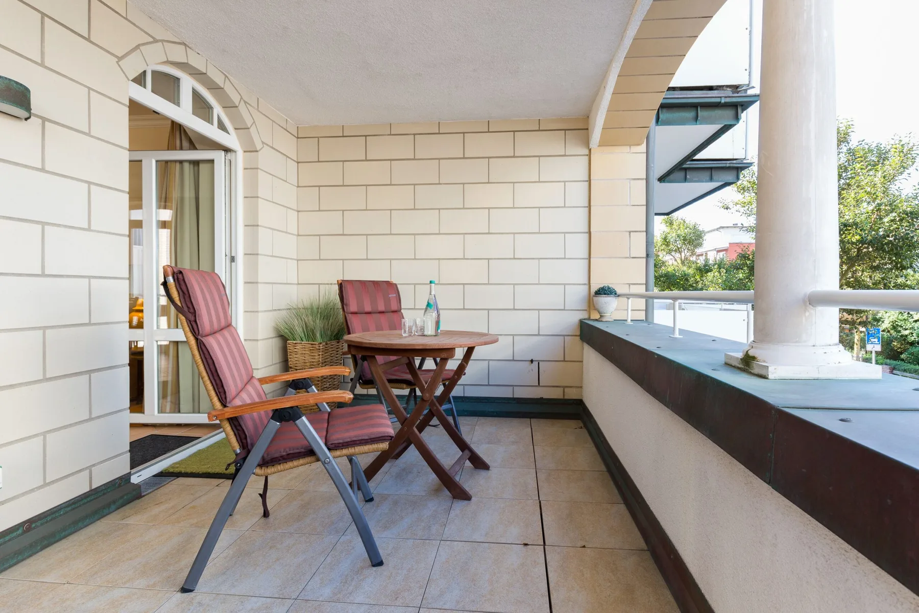 Un balcón cubierto con asientos y una mesa pequeña da a una zona verde.