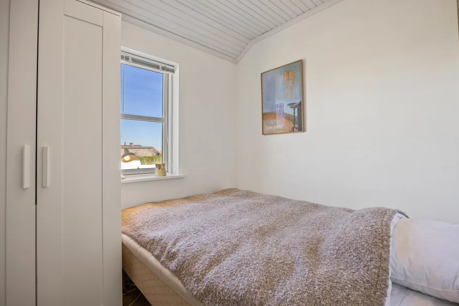 Un dormitorio con una cama bajo una ventana y un cuadro en la pared.