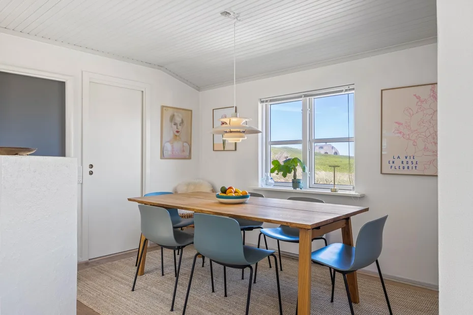 Un comedor luminoso con una mesa de madera, asientos azules y una ventana grande.