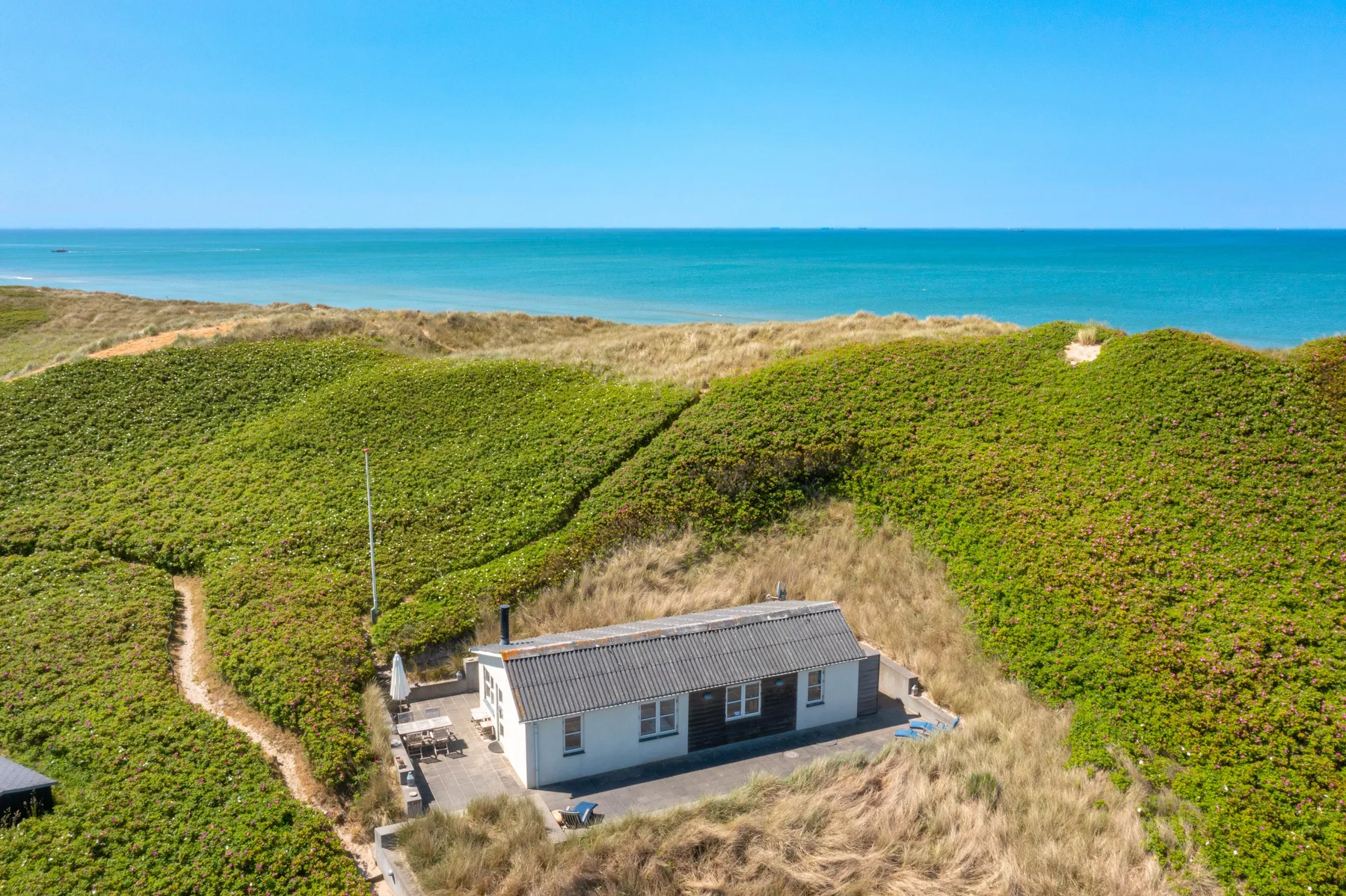 Una casa costera está entre dunas cubiertas de hierba con vistas al mar.