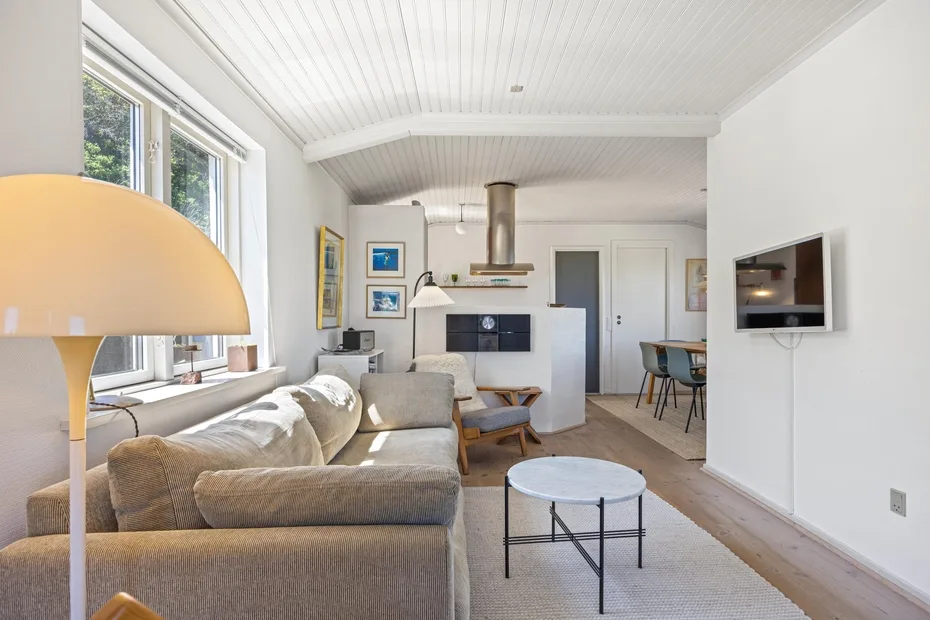 Una sala luminosa con asientos, un televisor y ventanas grandes.