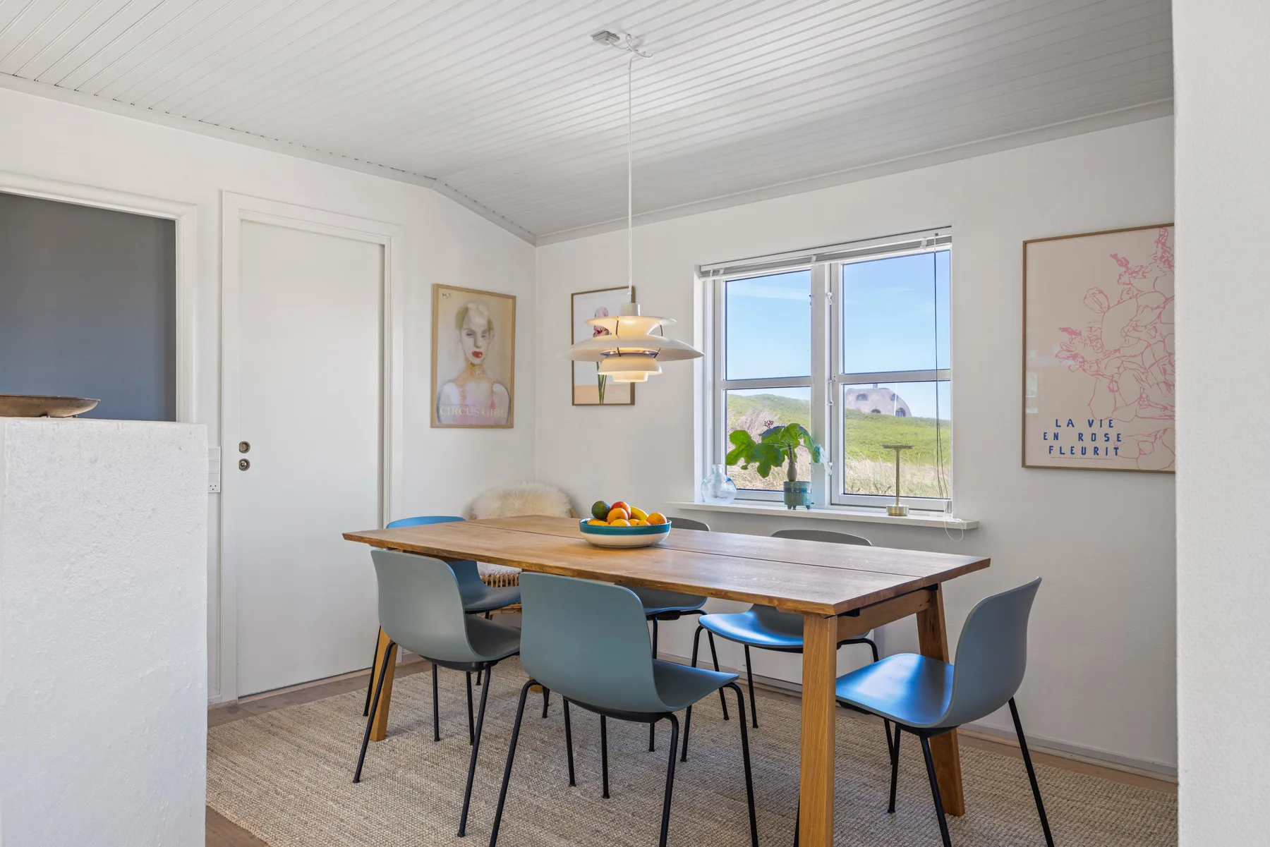 Un comedor luminoso tiene una mesa de madera, asientos y una ventana con vistas a zonas verdes.
