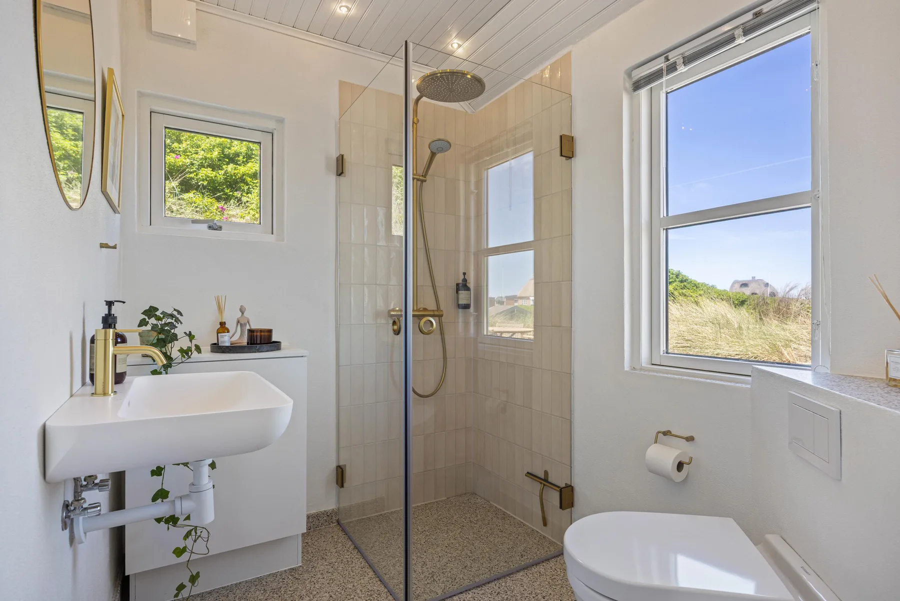 Un baño luminoso cuenta con una ducha de vidrio, un lavabo y una ventana.