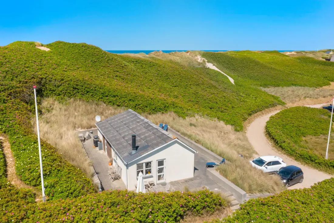 Una casa se encuentra entre dunas verdes junto a un sendero de arena.