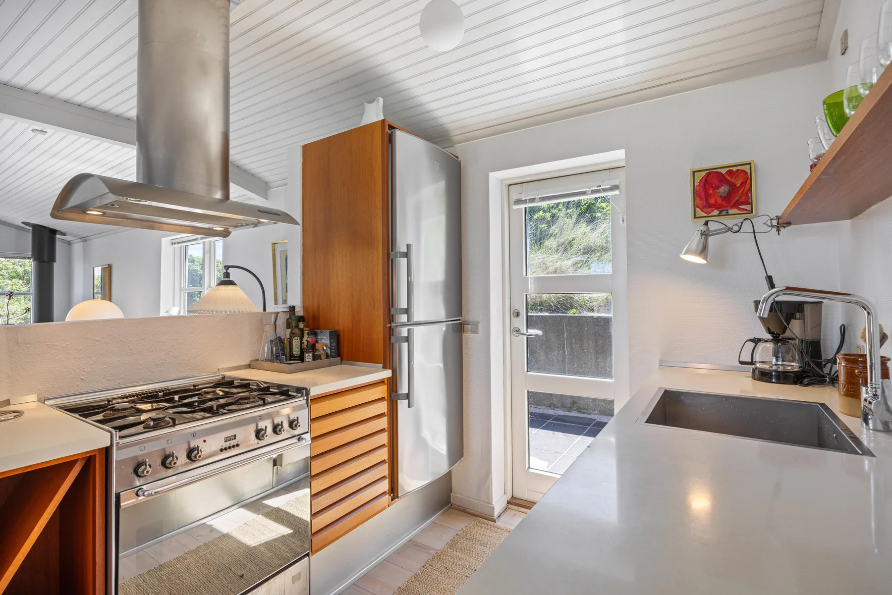 Una cocina luminosa con una estufa de gas, refrigerador y fregadero.