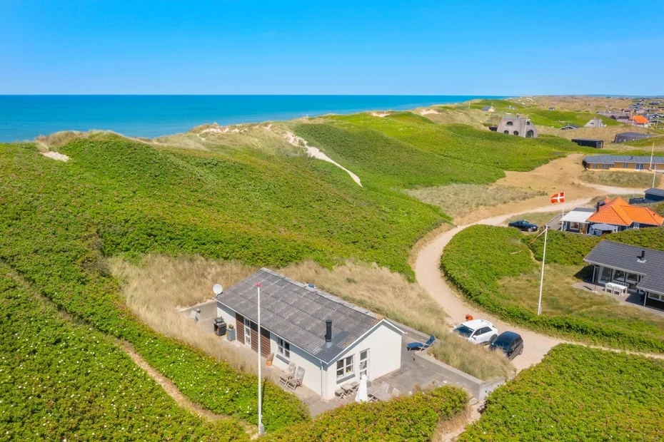 Vista aérea de casas costeras entre dunas verdes junto al mar.