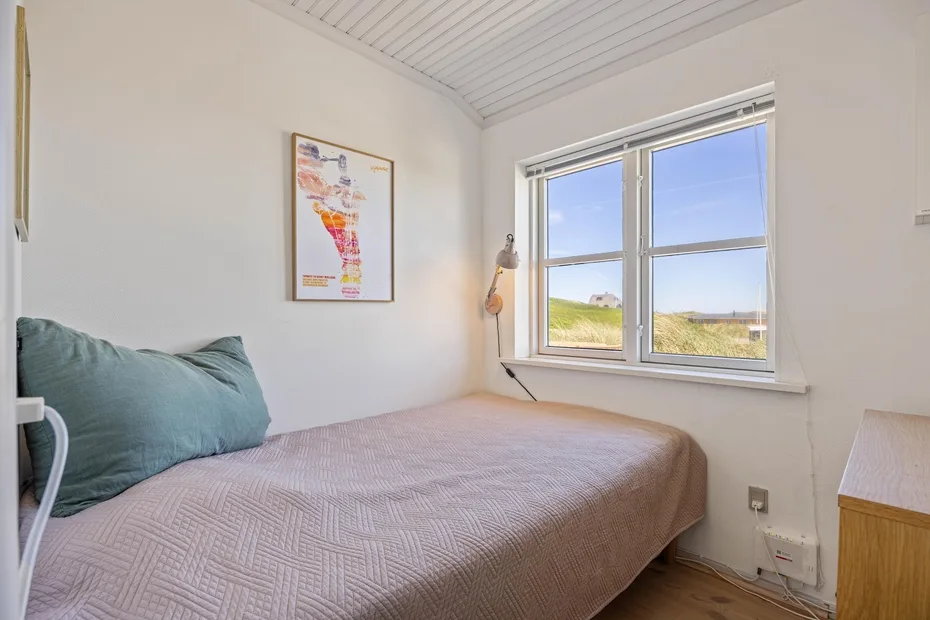 Un dormitorio con una cama junto a una ventana amplia con vistas a campos de hierba.
