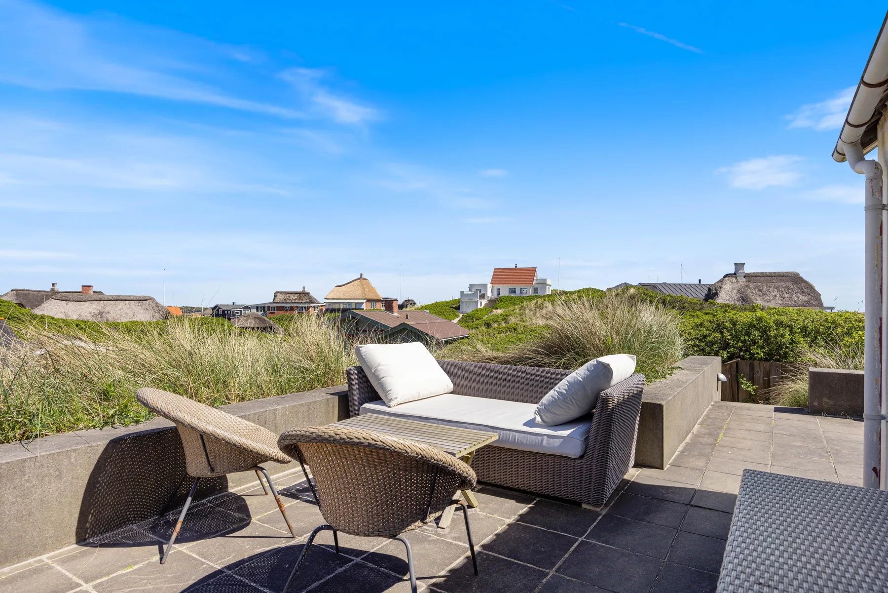 Una terraza en la azotea tiene asientos de mimbre y vistas a casas cercanas.
