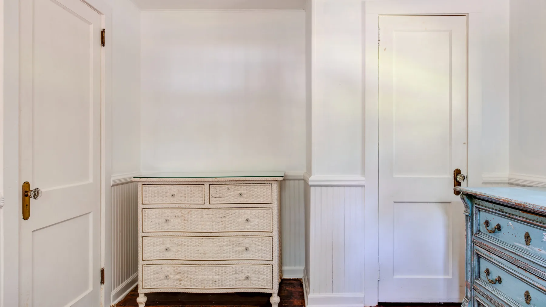 A bedroom corner with a light-colored dresser between two white doors.