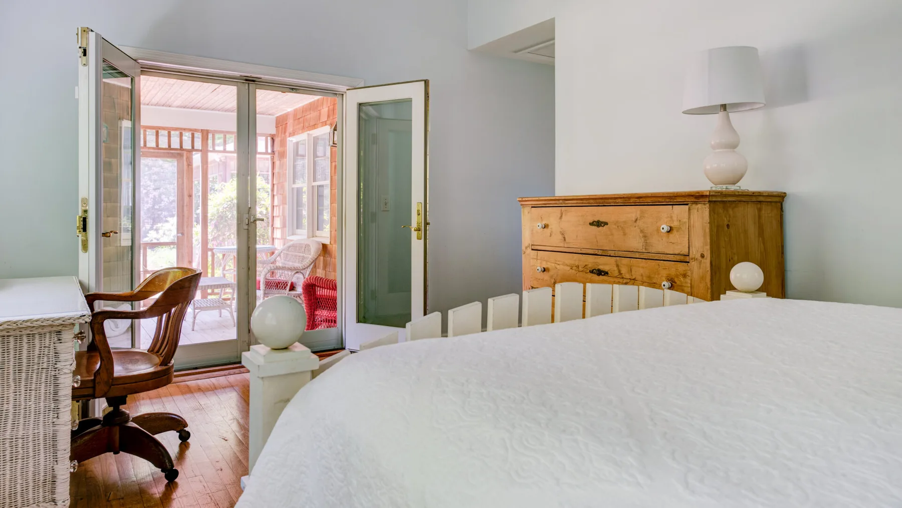 A bedroom with an open balcony doorway and a wooden dresser beside the bed.