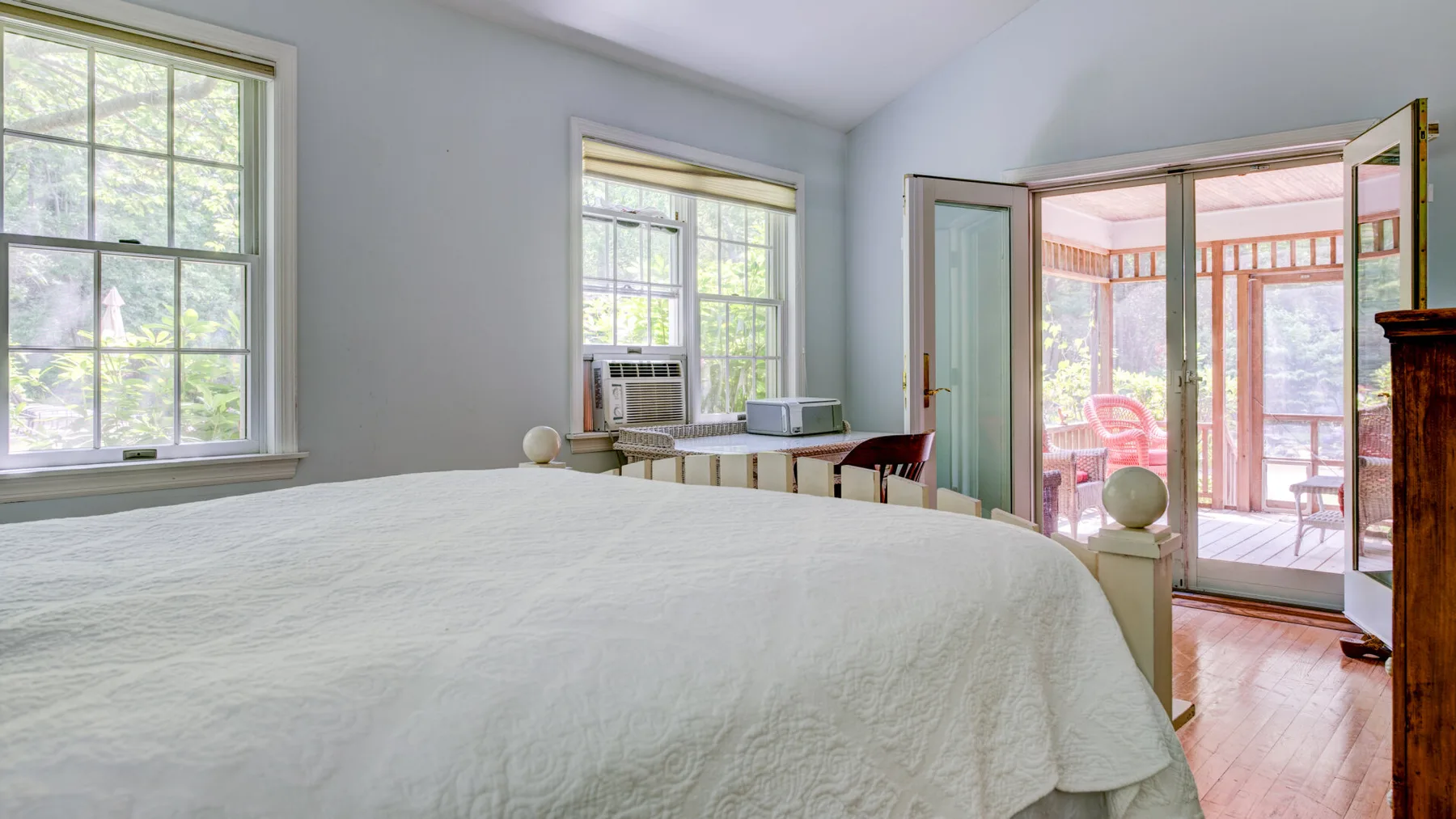 A bedroom with a large bed and windows opening onto a sunroom.