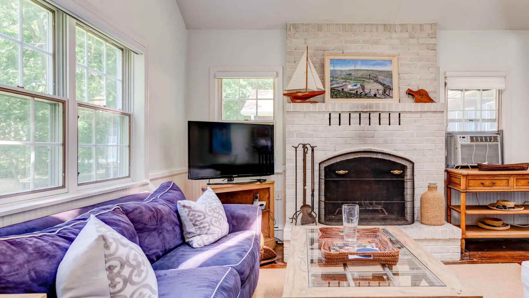 A bright living room with a purple sofa and a brick fireplace.