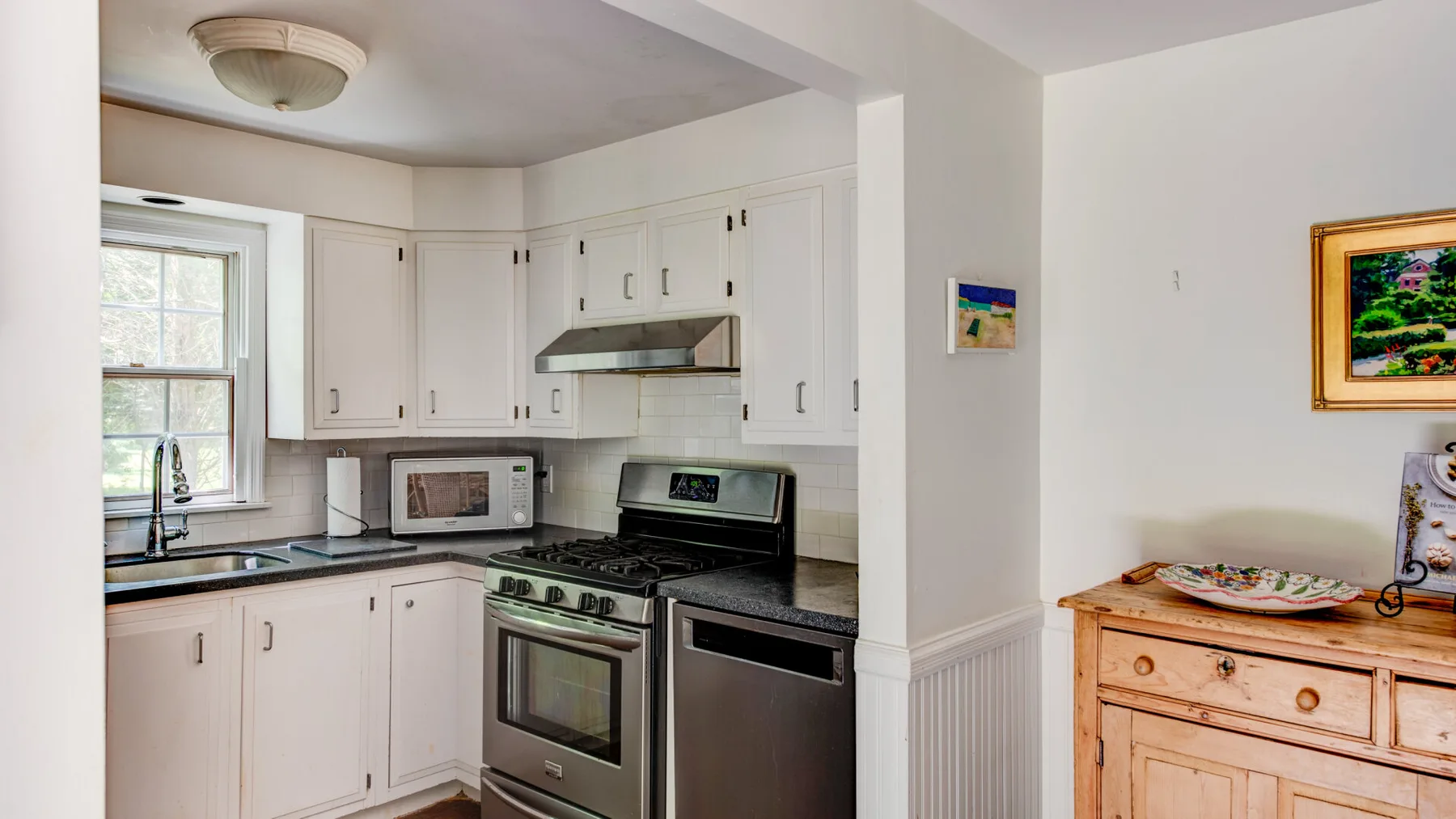 A bright kitchen with white cabinetry, a stove, and a window.