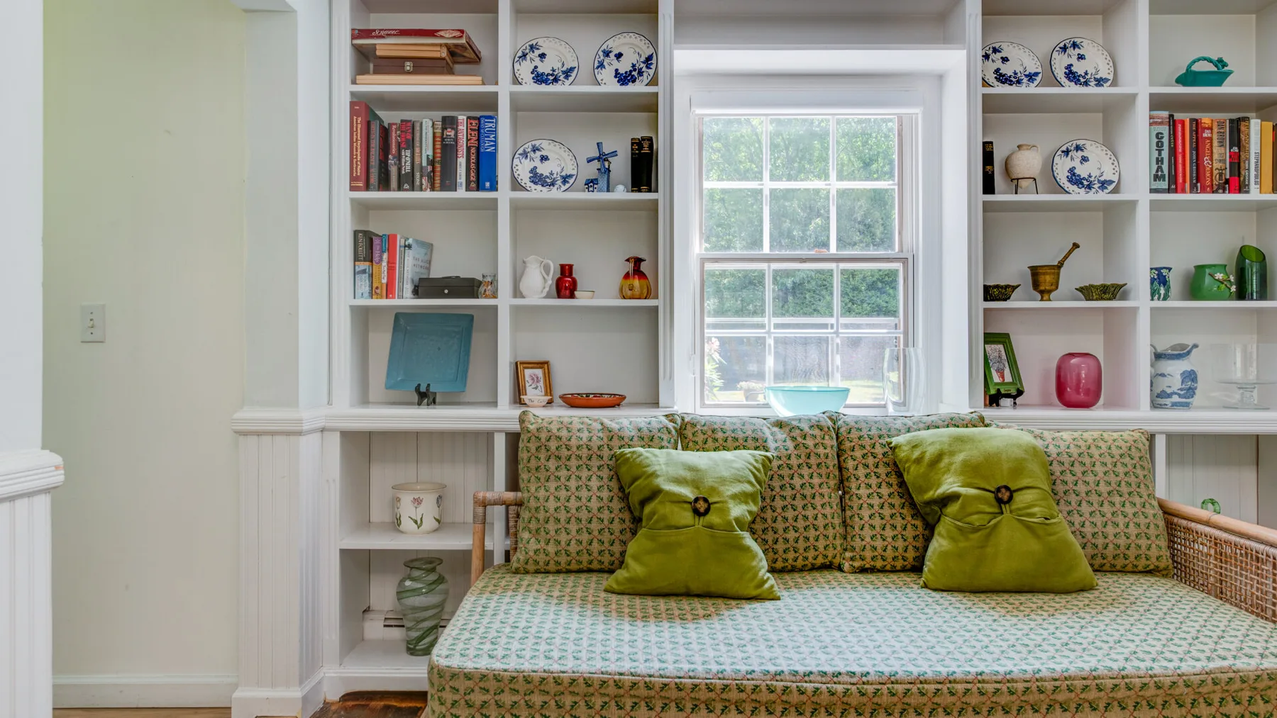 A sitting area with a patterned daybed and built-in shelves around a window.