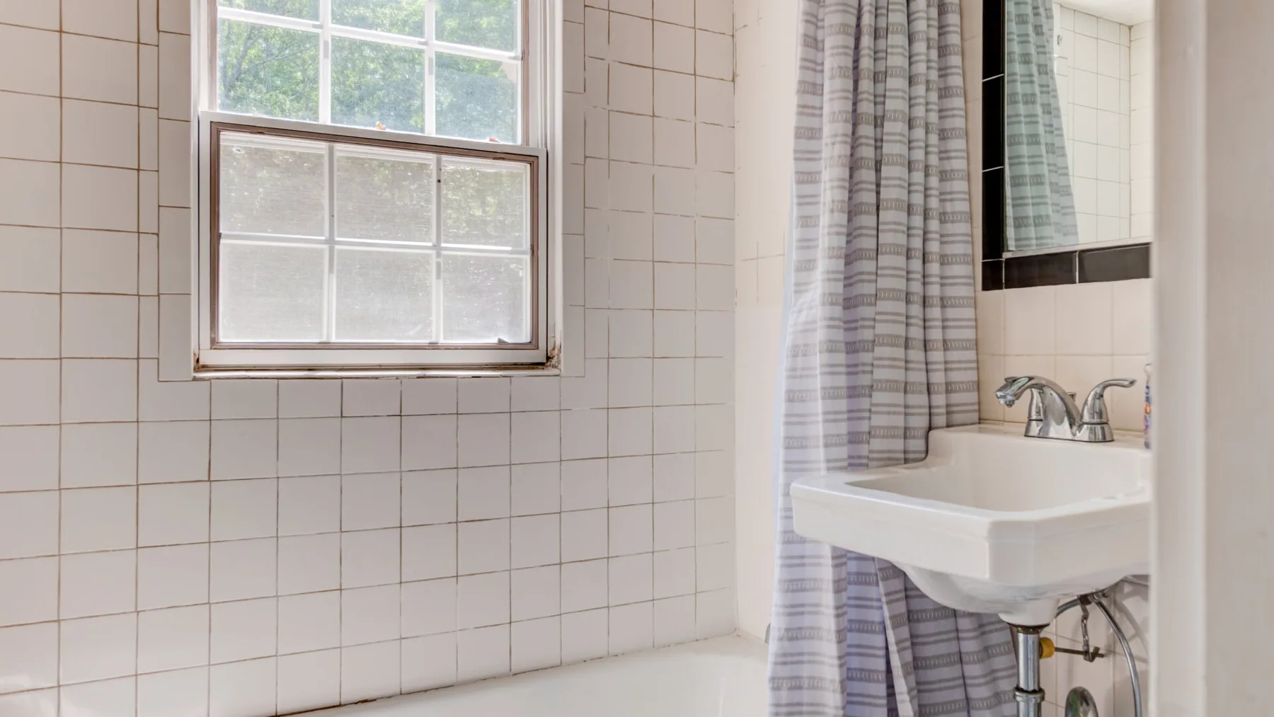 A tiled bathroom with a window, wall-mounted sink, and shower curtain.