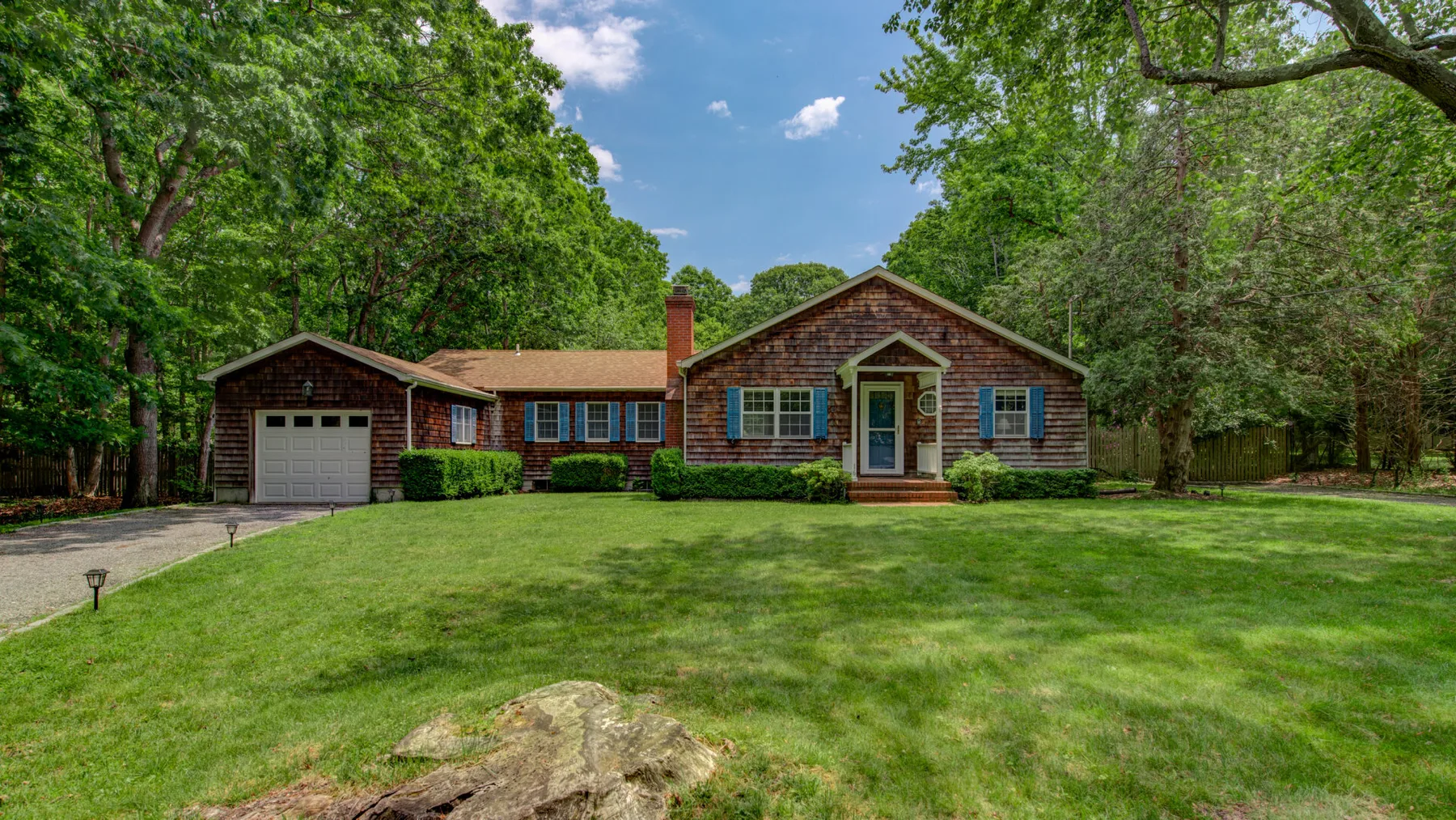 A brick house with an attached garage sits behind a broad green lawn.