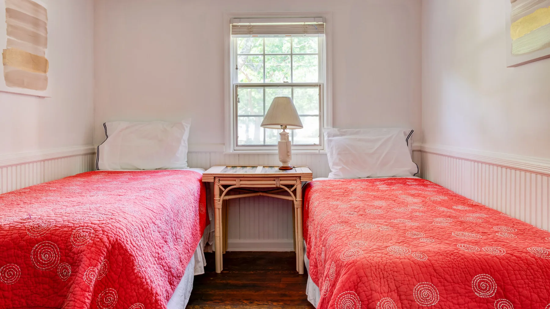 A bedroom with two beds covered in red quilts and a small table between them.