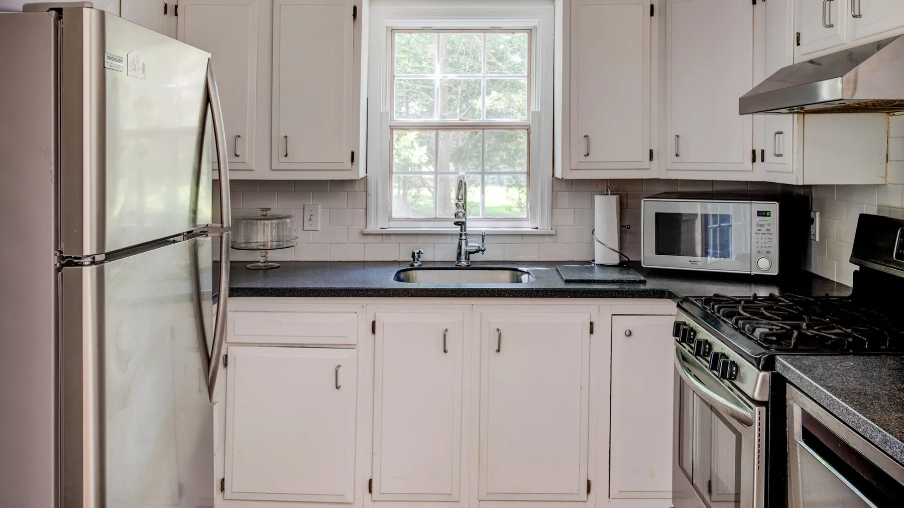 A bright kitchen with white cabinets, dark countertops, and a window above the sink.