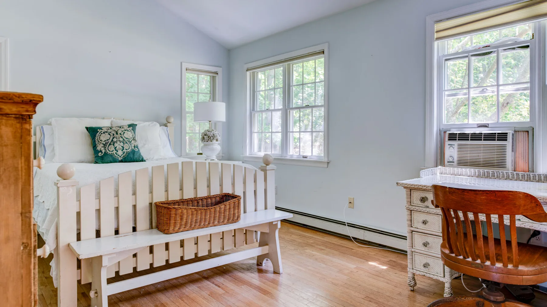 A bright bedroom with a white bed, large windows, and a wooden desk.
