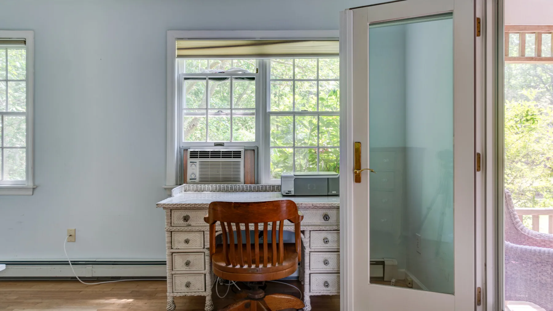 A bright room with a desk and wooden chair beside large windows.