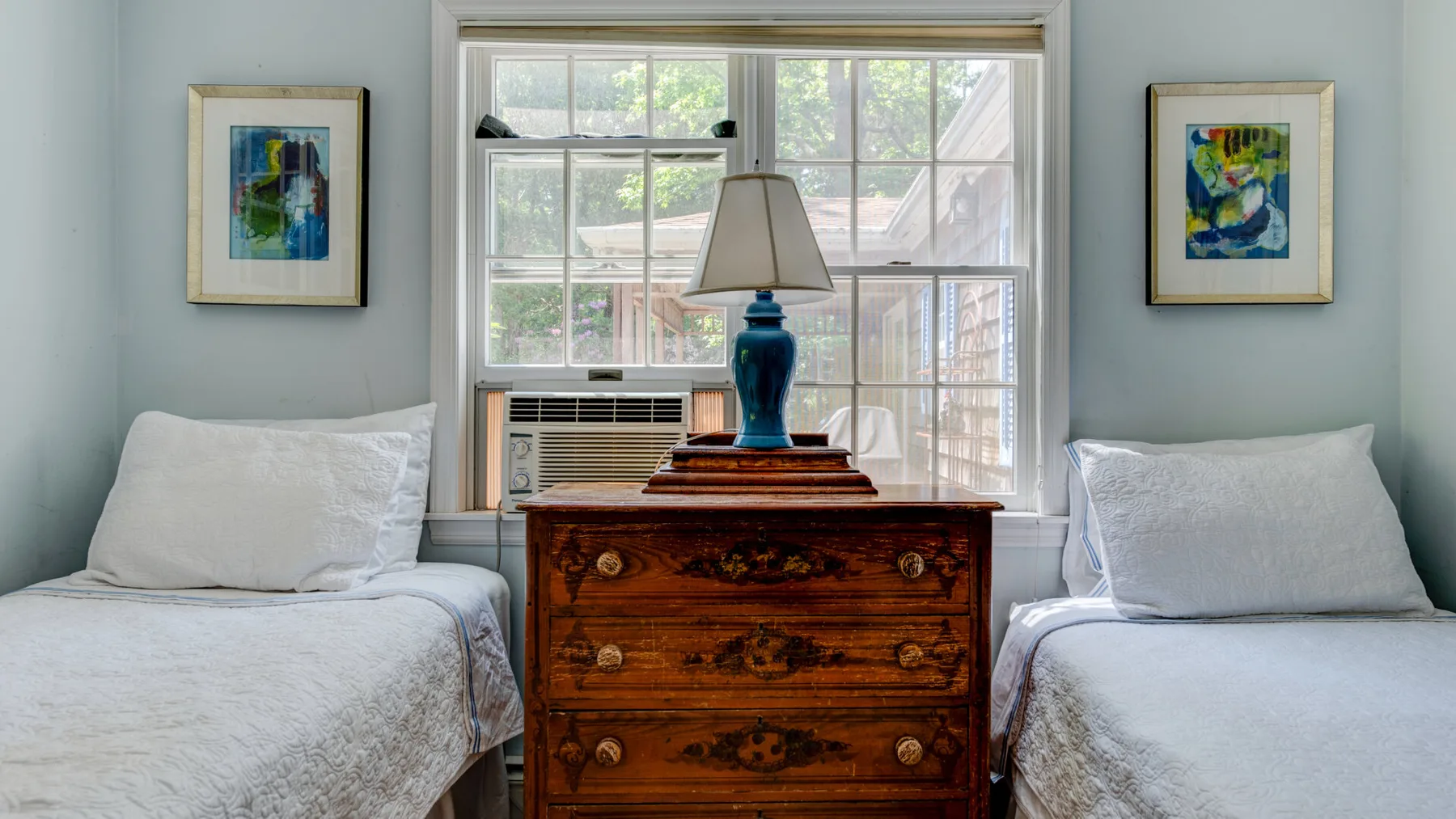 A bedroom with two beds and a wooden dresser beneath a window.