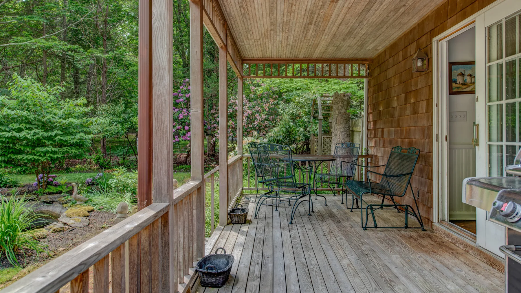 A covered wooden porch with outdoor seating overlooks a green garden.