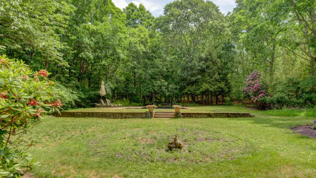 A grassy garden clearing is surrounded by trees and shrubs.