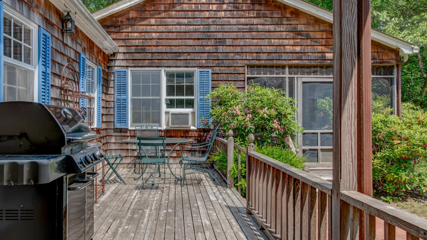 A wooden deck with outdoor seating, a grill, and a leafy shrub beside the house.