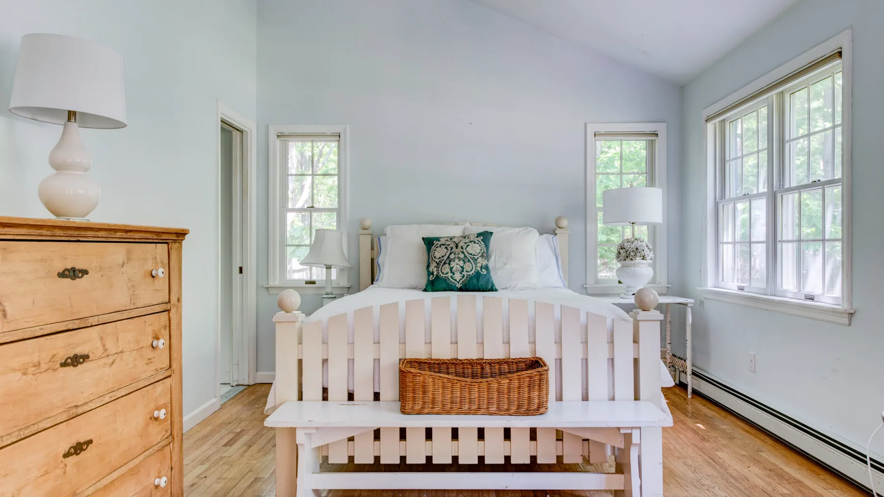 A bright bedroom with a white bed and large windows.
