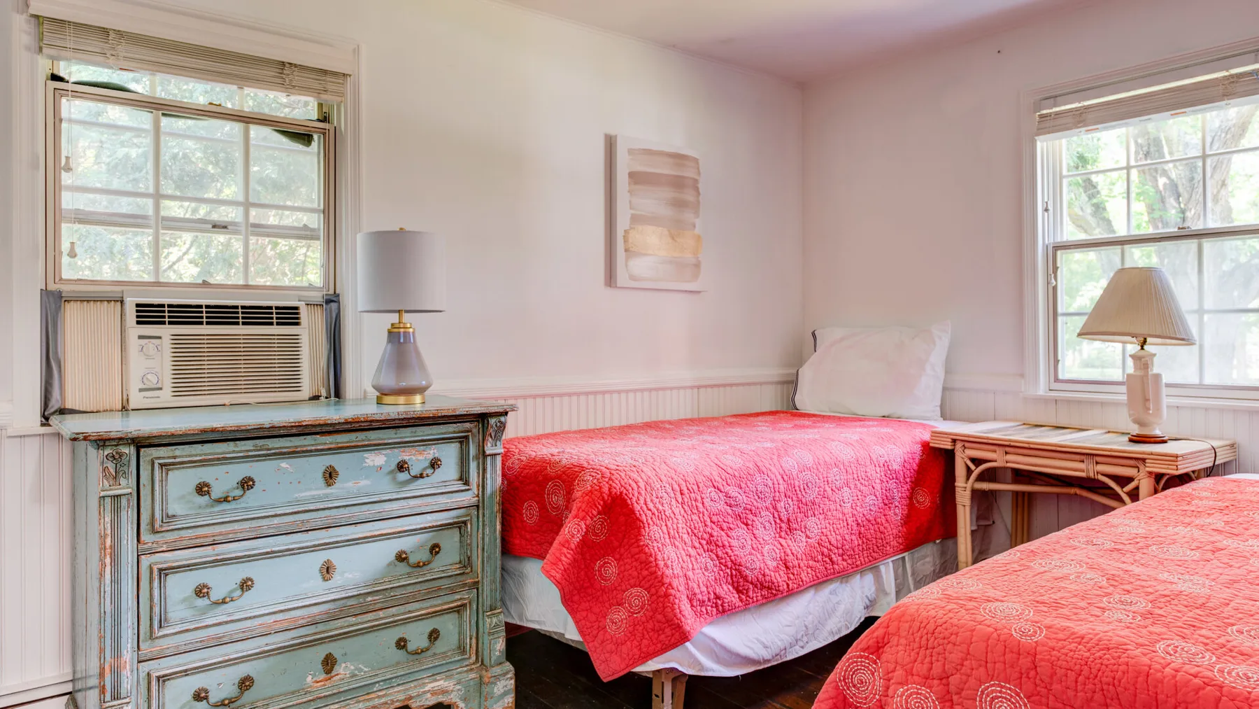 A bedroom with two beds covered in red quilts and a blue dresser.