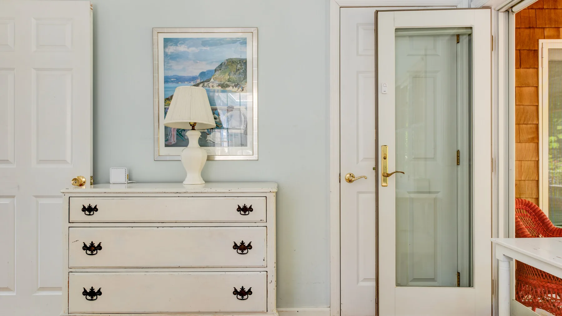 A light-colored dresser stands beside an open doorway with a glass-paneled door.