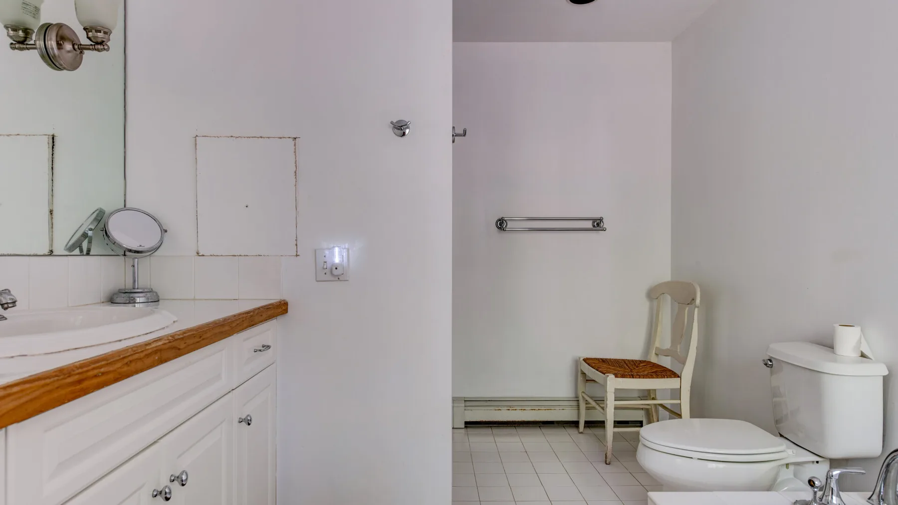A bathroom with a vanity, mirror, toilet, and a chair.
