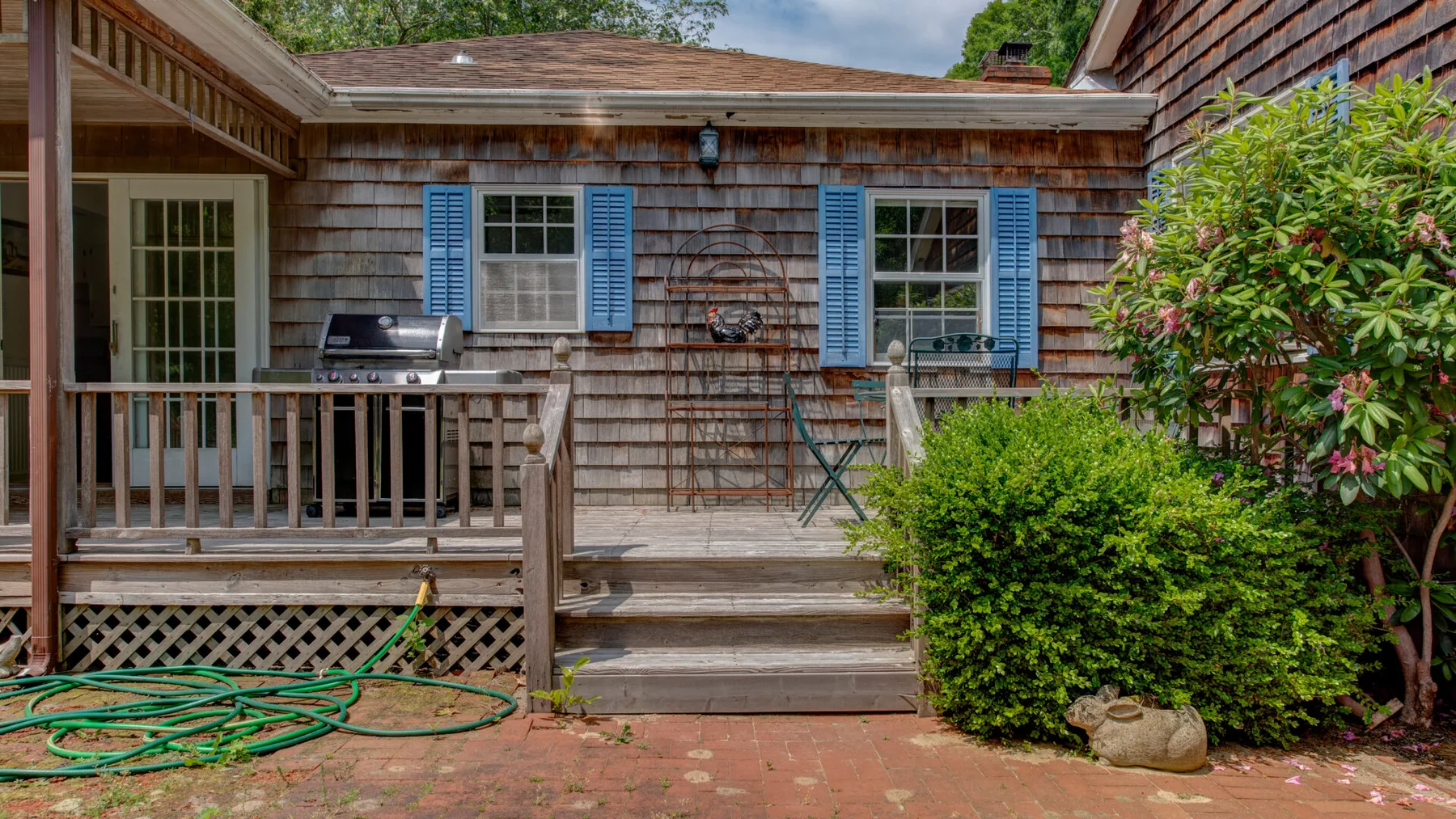 A wooden deck with outdoor seating and a grill beside the house.