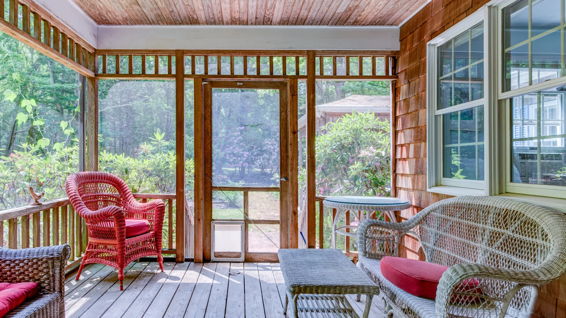 A screened porch with woven seating and views of greenery.