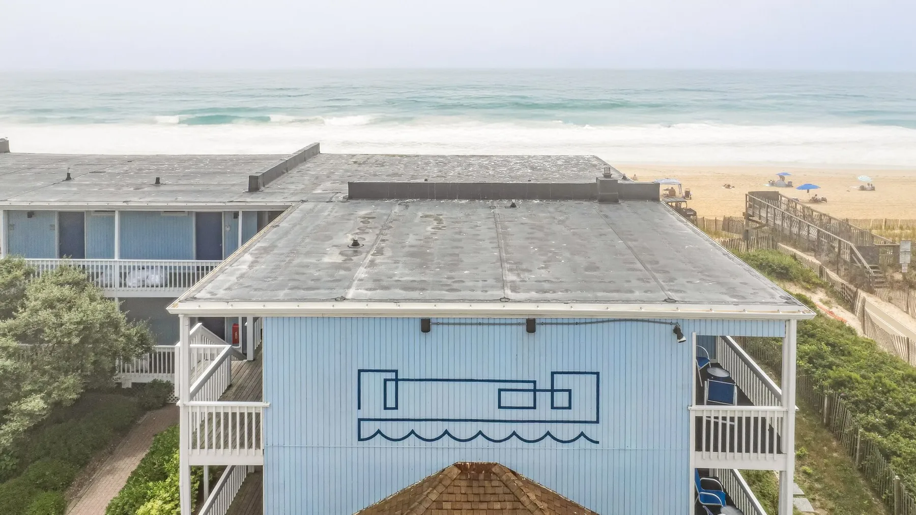 Un edificio junto a la playa mira al océano, con un mural geométrico azul en su fachada.