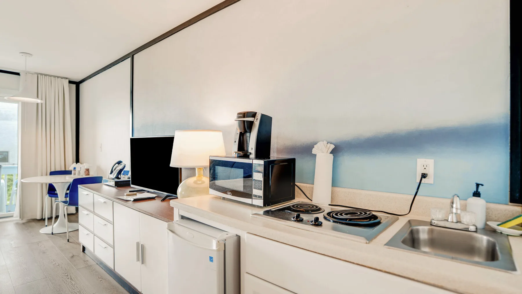 Una cocina pequeña y luminosa con encimera, placa de cocina, fregadero y zona de comedor.