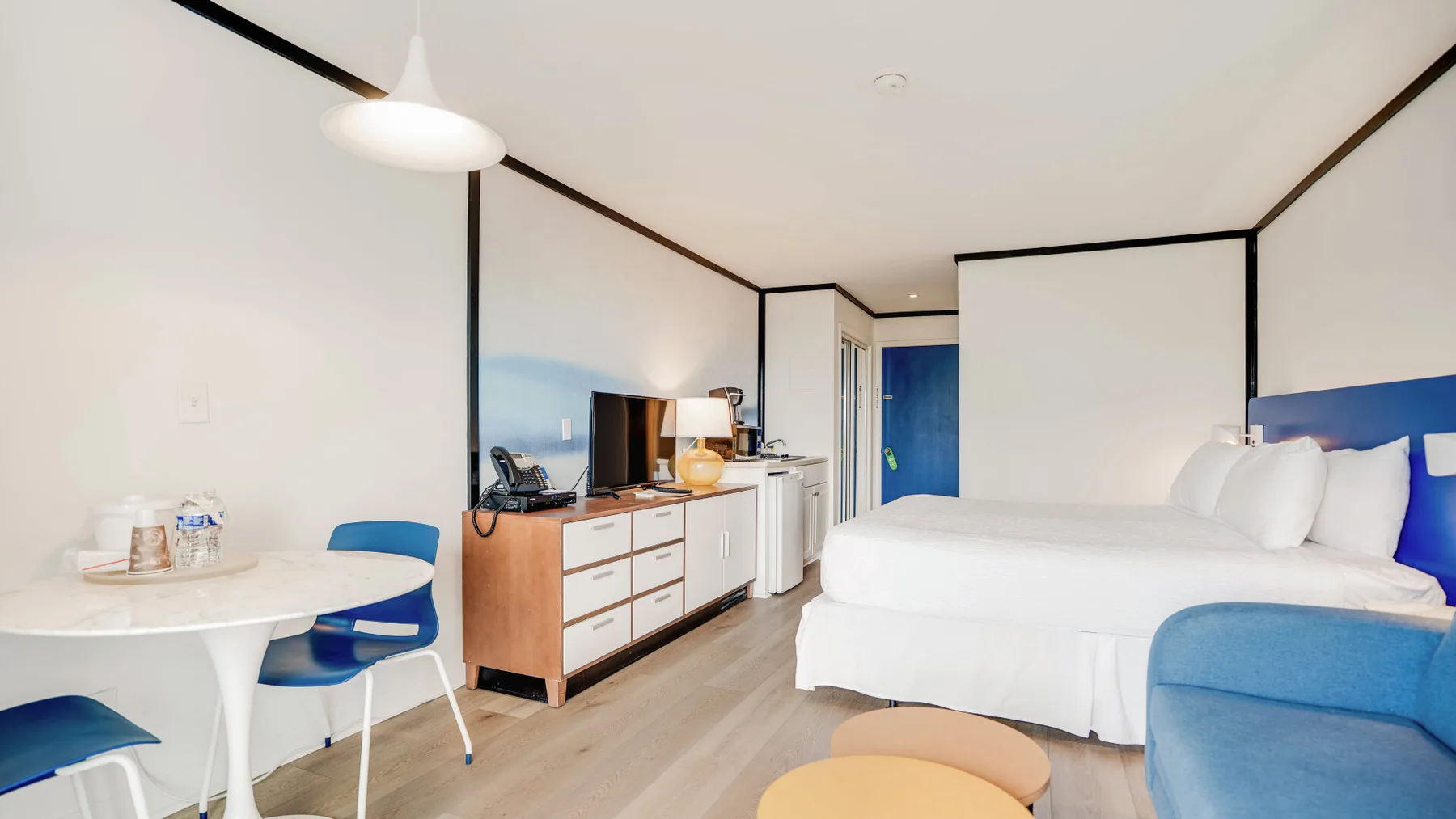 Una habitación de hotel luminosa con cama, asientos azules y mesa de comedor.