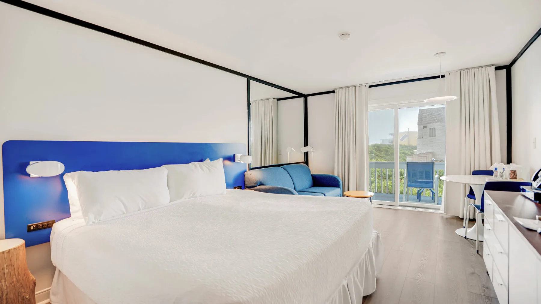 Un dormitorio con una cama grande, cabecero azul y asientos junto a una puerta de vidrio.