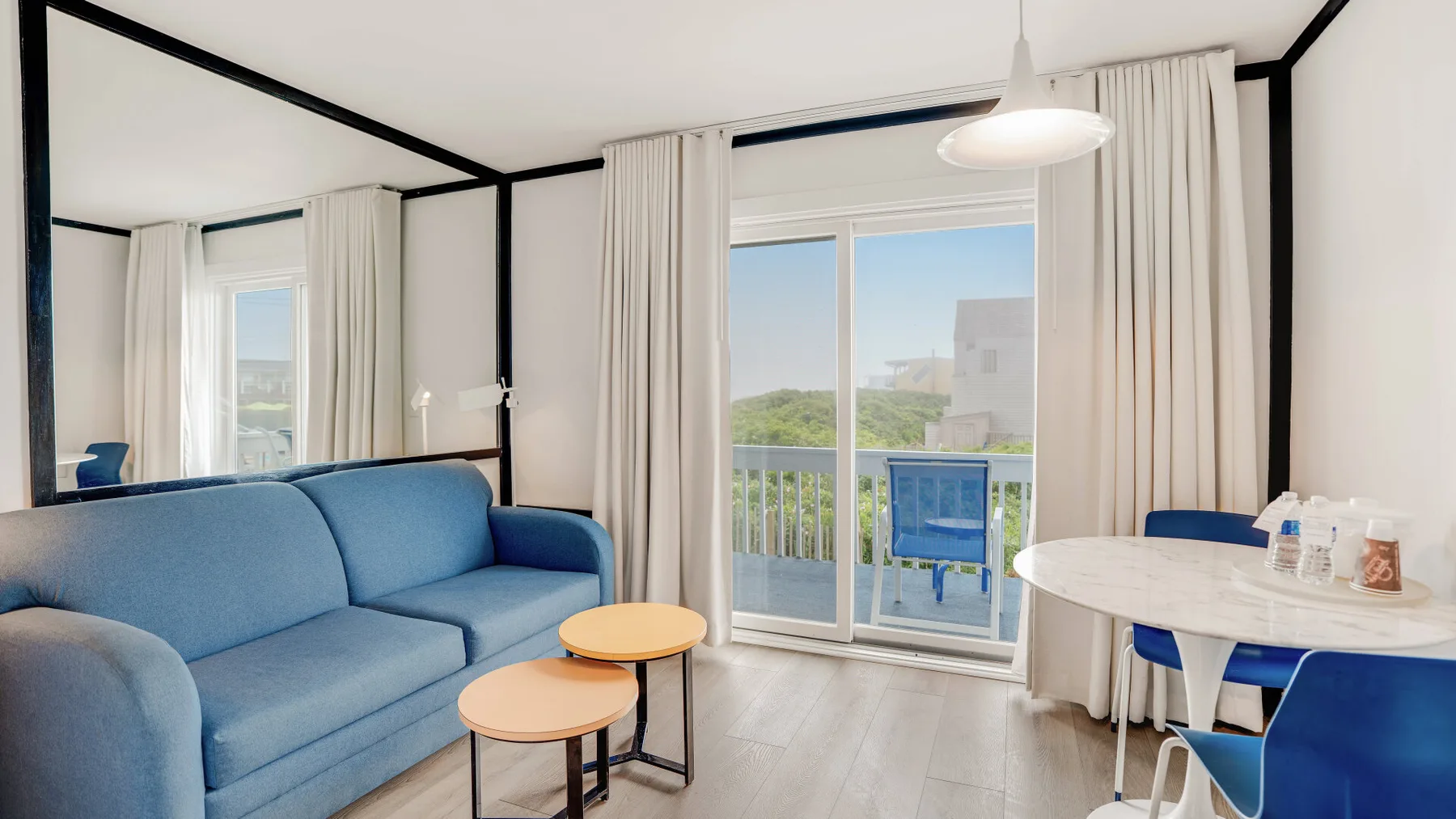 Una sala luminosa con asientos azules junto a grandes ventanas y una mesa de comedor.