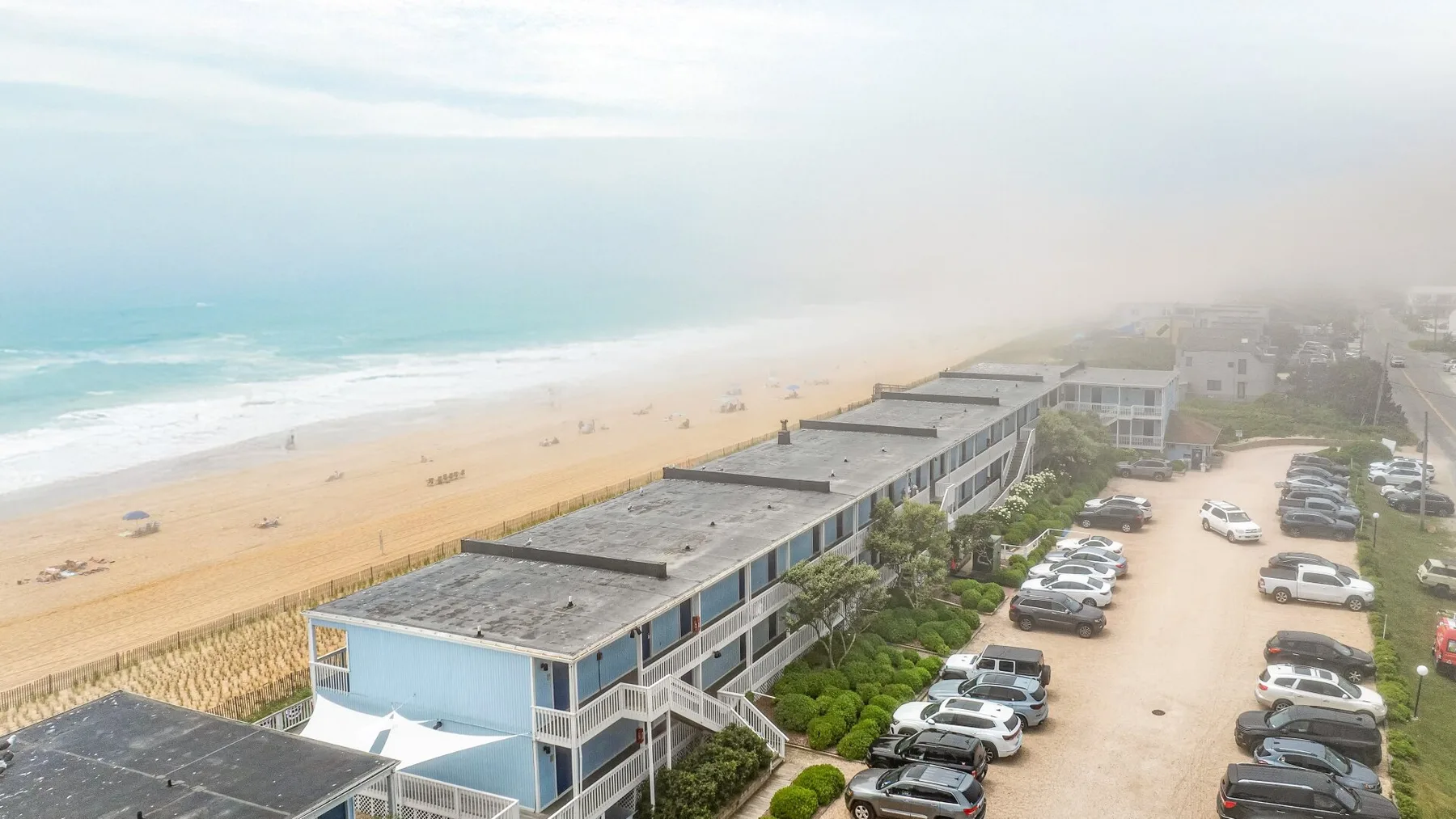 Vista aérea de edificios junto a la playa de arena y una zona de estacionamiento.