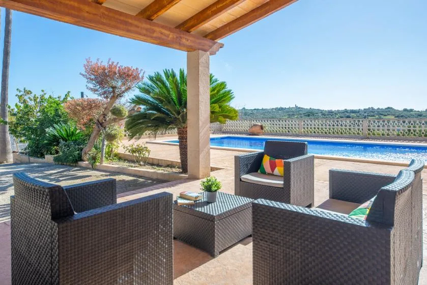 A covered outdoor seating area overlooks a swimming pool and landscaped garden.