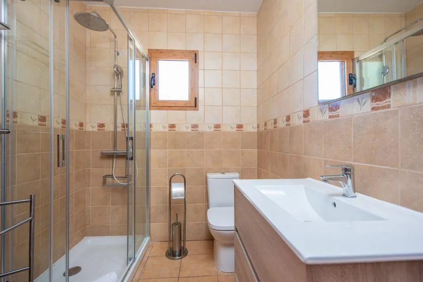 A tiled bathroom with a glass shower, toilet, and sink.