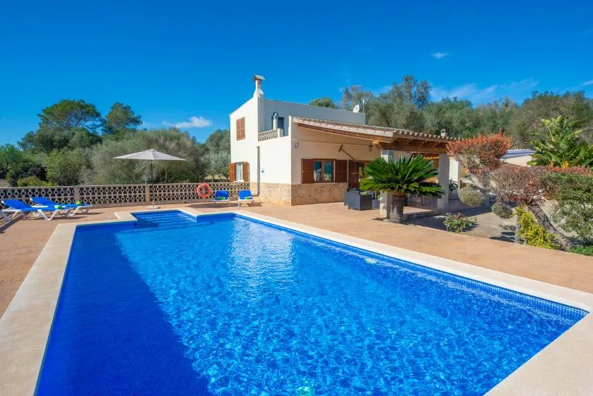 An outdoor swimming pool sits beside a house and patio seating.