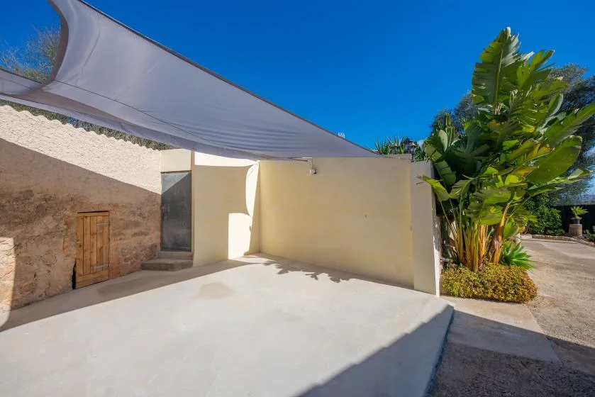 An outdoor patio with a fabric shade canopy and leafy plants.