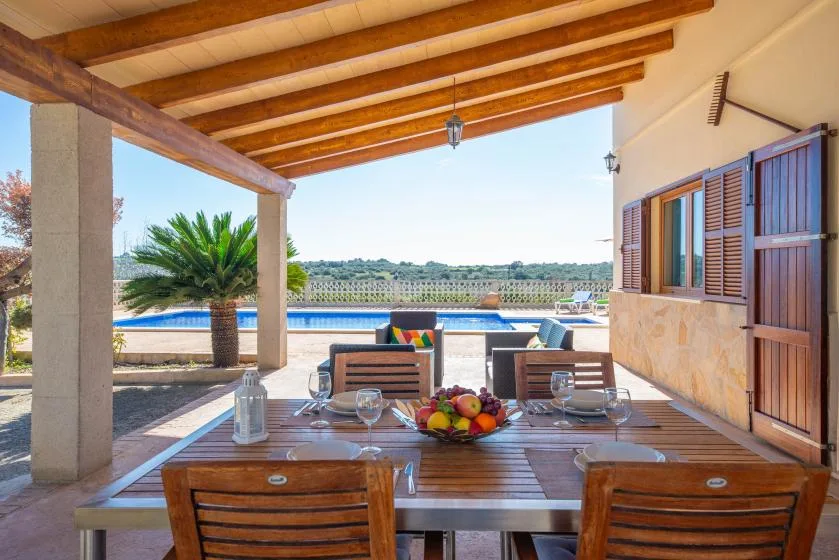 A covered outdoor dining area overlooks a swimming pool and landscaped grounds.