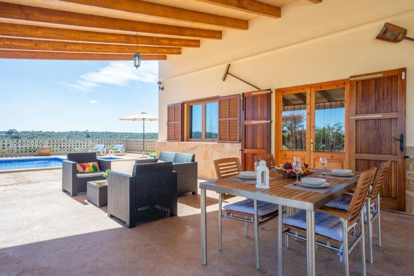 A covered outdoor dining area with a table and seating beside wooden doors.