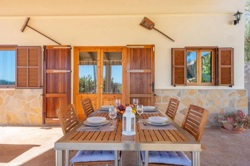 An outdoor dining area with a wooden table and chairs beside shuttered windows.
